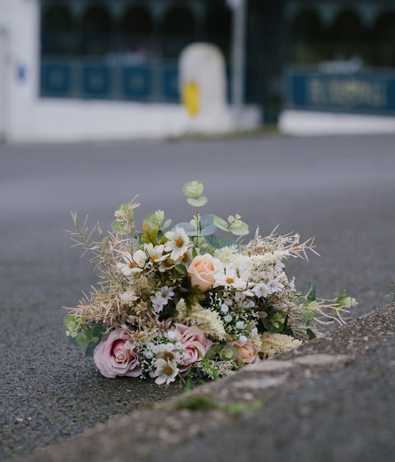 A delicate floral arrangement of fresh flowers, including soft pink roses, white daisies, and small white filler flowers, accented with light green eucalyptus and subtle foliage, lies on the ground be